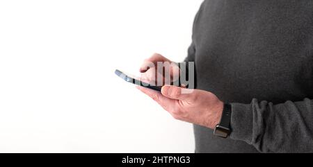 midsection of man holding smartphone in hand in front of white wall Stock Photo