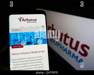 Person holding smartphone with website of Canadian company Arbutus Biopharma Corporation on screen with logo. Focus on center of phone display. Stock Photo