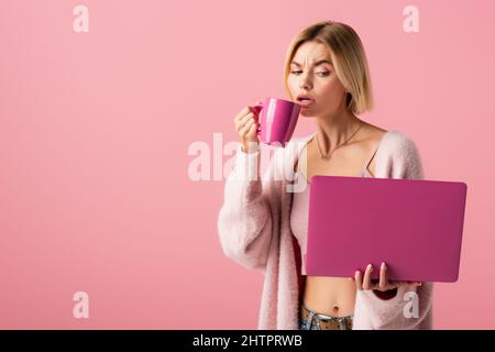 blonde woman holding mug with coffee and laptop isolated on pink,stock image Stock Photo