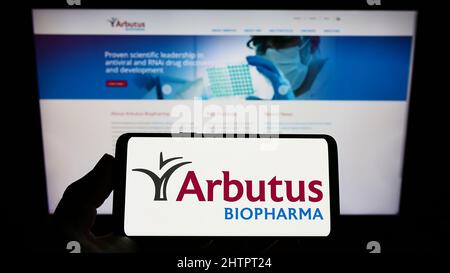 Person holding smartphone with logo of Canadian company Arbutus Biopharma Corporation on screen in front of website. Focus on phone display. Stock Photo