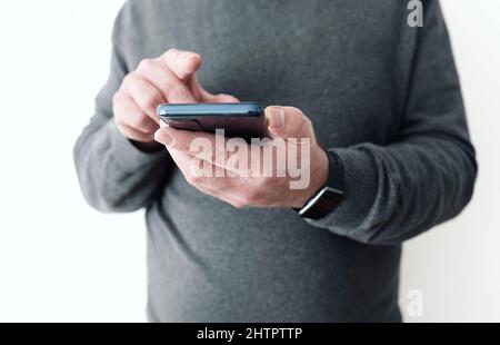 midsection of man holding smartphone in hand in front of white wall Stock Photo
