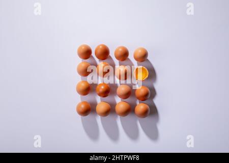 Overhead view of brown eggs with one broken egg arranged in square on table Stock Photo