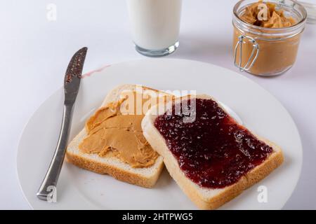 Close-up of open face peanut butter and jelly sandwich in plate by milk glass and jar on table Stock Photo