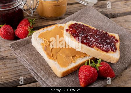 Close-up open face peanut butter and jelly sandwich on napkin with jars and strawberries at table Stock Photo