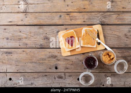 Overhead view of open face peanut butter and jelly sandwich on serving board with jars at table Stock Photo