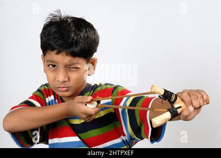 Mumbai Maharashtra India July 22 2006 - Eight Years Old Indian Little Boy Smiling Playing with Traditional Catapult or slingshot on White Background. Stock Photo