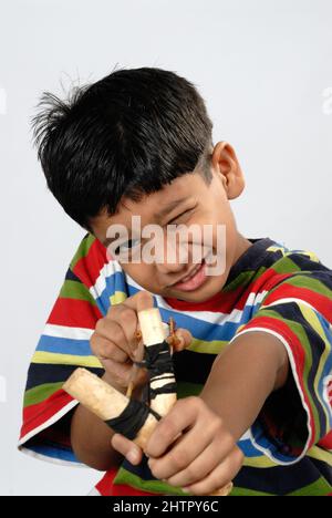 Mumbai Maharashtra India July 22 2006 - Eight Years Old Indian Little Boy Smiling Playing with Traditional Catapult or slingshot on White Background. Stock Photo