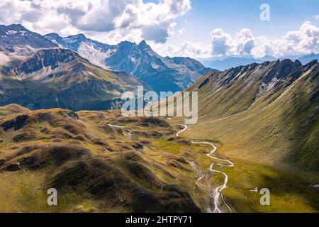 Aerial view towards the Capanna Motterascio, an alpine hut on the Greina plateau in Blenio, Swiss Alps. A rocky ridge on the right leads the eye towards the river that flows sinuously in the valley. Stock Photo