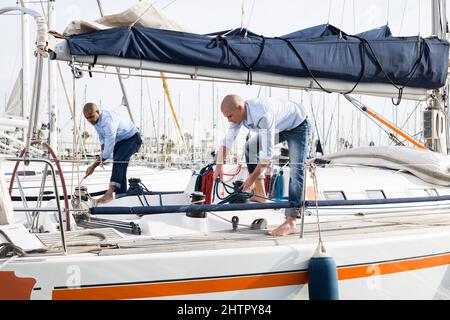 Two young men in blue shirts tidy up private sailing yacht in the seaport  Stock Photo - Alamy