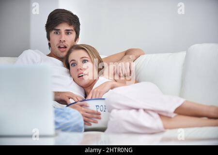 This is too tense. Shot of a young couple watching a scary movie at home. Stock Photo