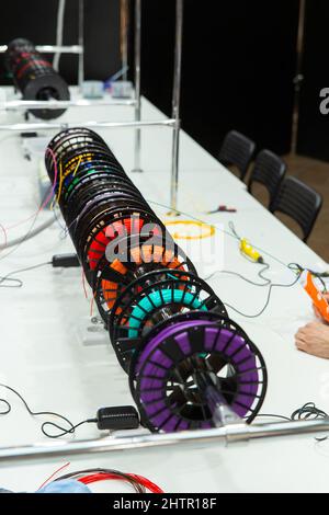 Colorful rainbow plastic filaments on bobbins and some 3D pens laying on white background. Visitors to the exhibition of modern technologies test 3D p Stock Photo