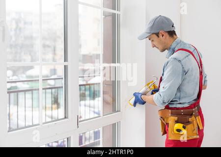 Construction worker putting sealing foam tape on window in house Stock Photo
