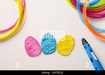 Creative colorful eggs of popular plastic for Easter holiday. Rainbow plastic filaments with 3D pen laying on white background. New toy for child. Top Stock Photo