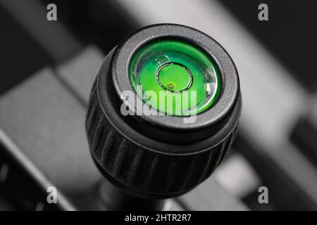 The bubble level of a photographic tripod is filled with green liquid. Macro photography