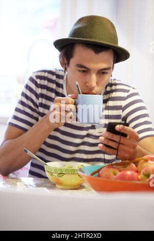 Enjoying a quick cup of coffee - Morning routine. Young guy texting while drinking his coffee at home. Stock Photo