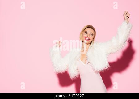 excited blonde woman in slip dress and faux fur jacket holding shopping ...