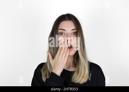 Shocked girl covering mouth with hand. 'Is that for real?!' concept photo on white background. She is looking right.  Text space. Stock Photo