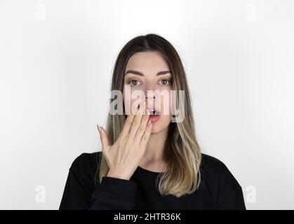 Shocked girl covering mouth with hand. 'Is that for real?!' concept photo on white background. She is looking right.  Text space. Stock Photo