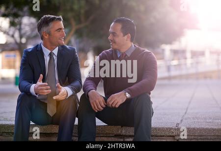 So you see.... Shot of two businessmen having a discussion while sitting outside. Stock Photo