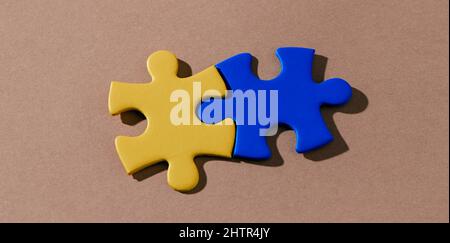 high angle view of two puzzle pieces painted in yellow and blue forming the ukrainian flag on a brown background, in a panoramic format to use as web Stock Photo