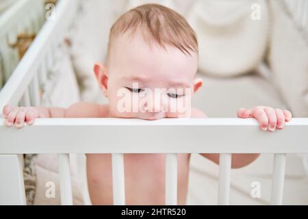 Baby gnaws at the edge crib during teething itching. Funny child scratching his teeth on the rail bed, age six months Stock Photo