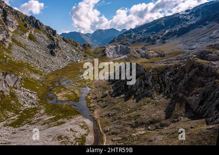 Aerial view towards the Piani della Greina, at the Passo della Greina, a mountain pass in Blenio, Switzerland. A rocky ridge on the right leads the eye towards the river that flows in the valley.  Stock Photo