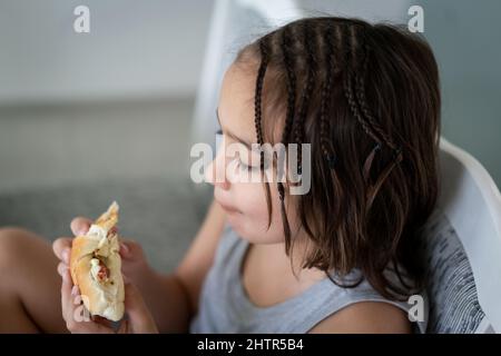 Little boy eating sandwich while sitting at desk in kitchen. High quality photo Stock Photo