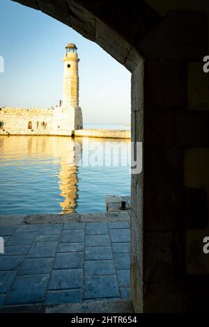 Old lighthouse view through a medieval arch in the Venetian harbour at sunset, Rethymno, Crete, Greece Stock Photo