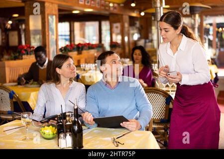 Polite young waitress taking order from couple in restaurant Stock Photo
