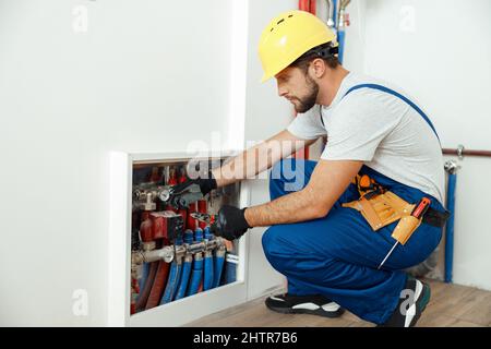 Serious technician, plumber in uniform checking water consumption, pipes and meter counter in apartment Stock Photo