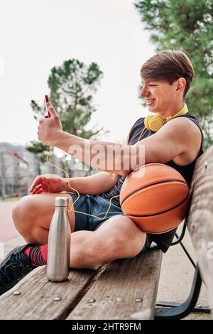 basketball player resting. male athlete sitting while making a video call on his mobile phone. Stock Photo