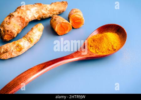 Ground Turmeric with Fresh Turmeric Root: A spoonful of ground turmeric with raw turmeric in the background Stock Photo