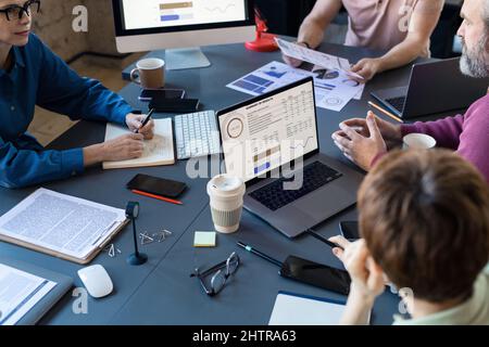 Close-up of group of people sitting at the table at meeting and discussing presentation with graphs on the screen Stock Photo