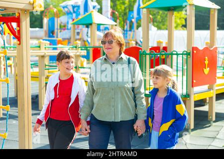 Grandmother walks with her grandchildren on playground Stock Photo