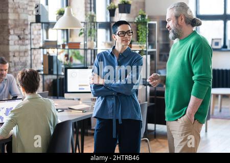 Businessman talking to businesswoman while they standing at board room during business meeting with colleagues Stock Photo