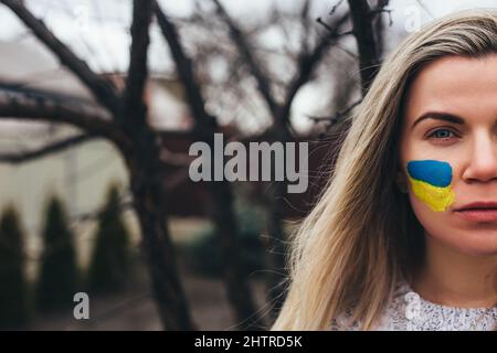Outdoor portrait of young girl with blue and yellow ukrainian flag on her cheek. Stop war in Ukraine. Russia stop war. Stock Photo