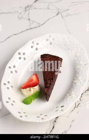 https://l450v.alamy.com/450v/2htrf1g/chocolate-cake-on-a-white-marble-table-a-piece-of-brownie-on-a-white-plate-with-strawberry-and-cream-serving-dessert-selected-focus-2htrf1g.jpg