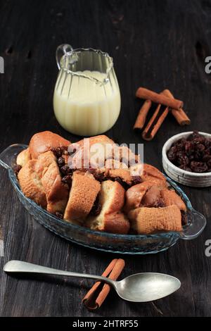 Cinnamon Vanilla Bread and Butter Pudding with Raisins in Clear Baking Dish, Served with Vla. On Wooden Table Stock Photo