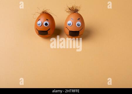 Doodle eyes, eyebrow and mask drawing on easter eggs with strings on top against orange background Stock Photo