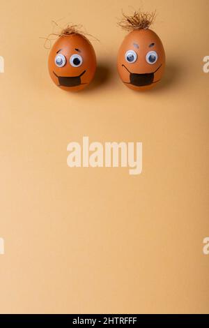 Eater eggs with doodle eyes, eyebrow, mask drawing and strings on top against orange background Stock Photo