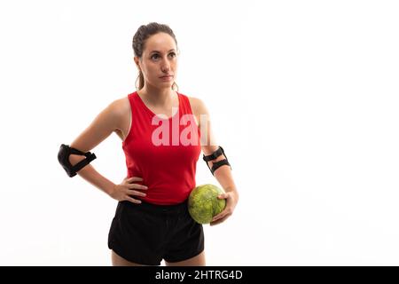 Caucasian young female handball player looking away while standing with ball and hand on hip Stock Photo