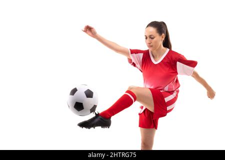 Caucasian young female soccer player kicking ball while playing soccer against white background Stock Photo