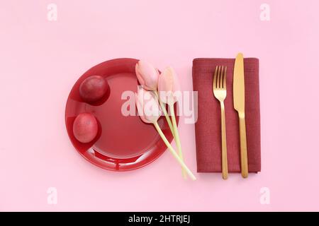 Beautiful table setting with red Easter eggs and tulips on pink background Stock Photo