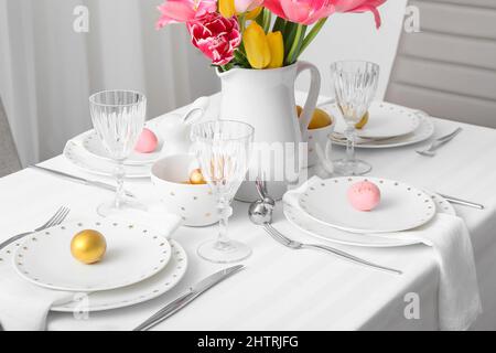 Beautiful table setting with Easter eggs and tulips in room Stock Photo