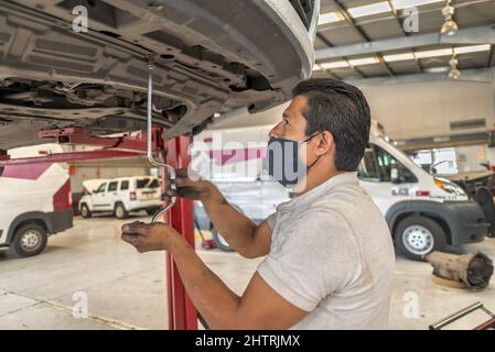 Latin male mechanic working on the bottom of a car removing parts Stock Photo