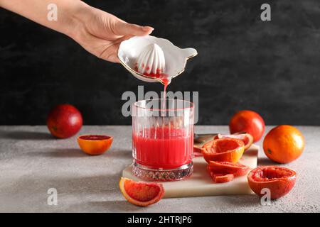 Woman pouring grapefruit juice from juicer into glass on grey background Stock Photo