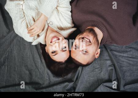 Beautiful girl and wonderful guy laughing. They lie side by side on the eve of Valentine's Day or New Year. Gray fabric background. Soft focus. Inverted photo. Stock Photo