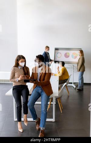 Handsome young African American business man and cute business woman working on digital tablet while wearing a facial protective masks Stock Photo