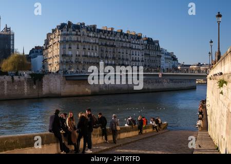 Paris, France - February 27, 2022 : Tourists sitting next to the river Seine and a a picturesque scenery of Paris in the background Stock Photo