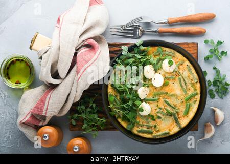 Omelet with spinach, green beans, potato and spinach healthy food in black frying pan on grey stone old rustic background. Traditional frittata for br Stock Photo